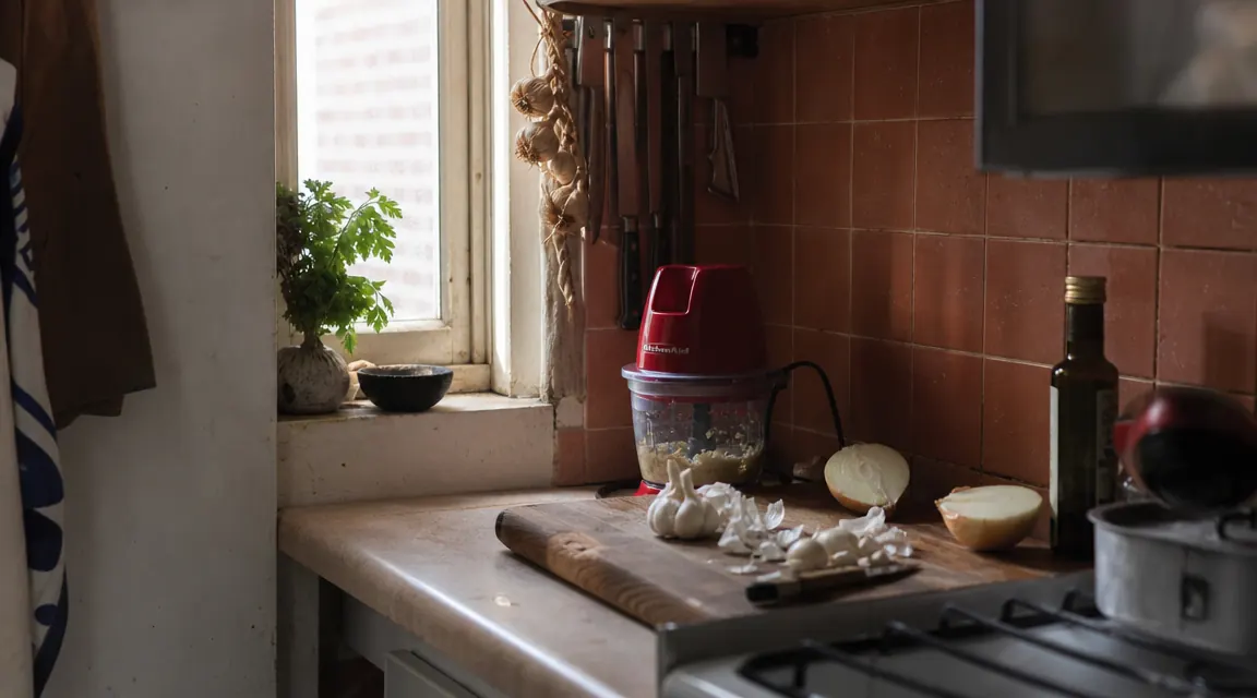 Small white kitchen counter with a compact food chopper next to a cutting board and fresh garlic and onions