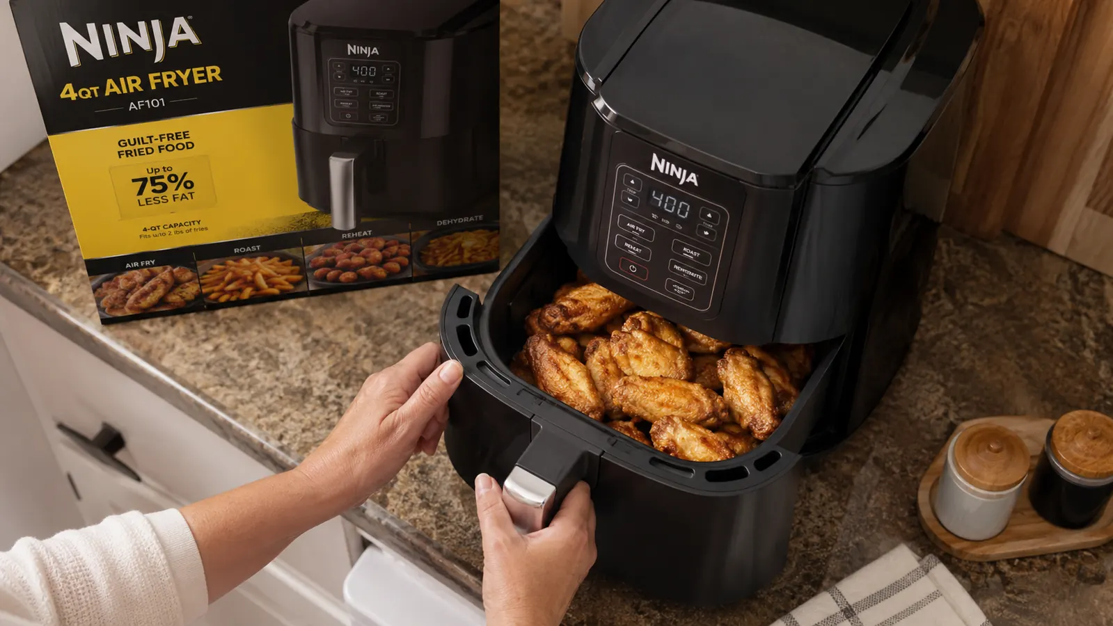 Hand pulling out the Ninja Air Fryer basket revealing crispy golden chicken wings inside