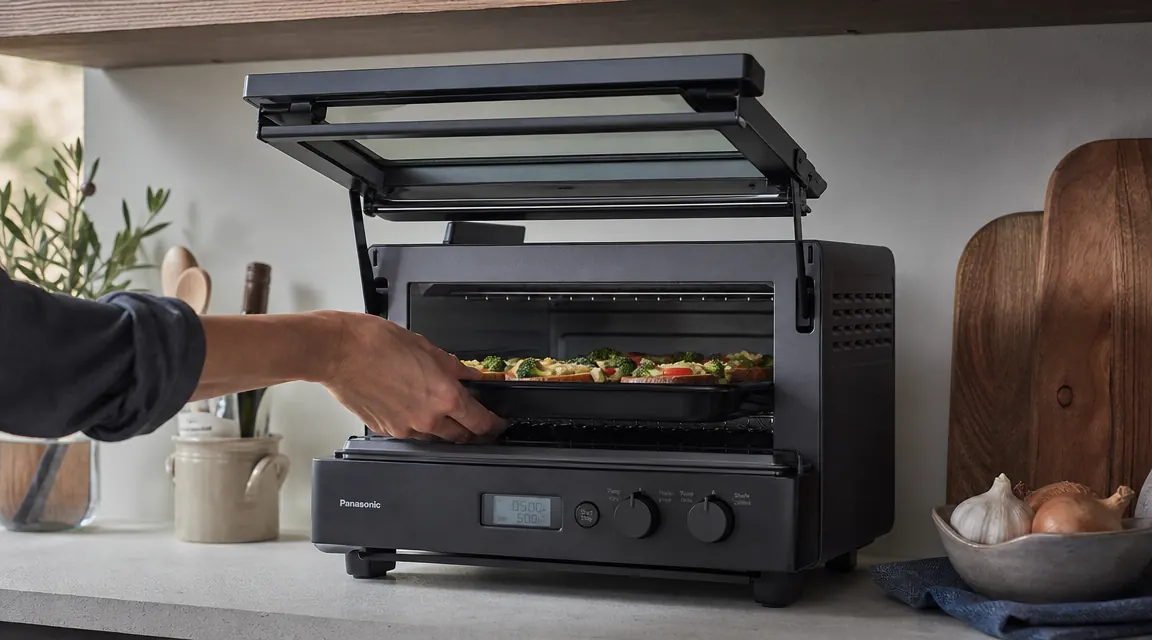Side view of Ninja Flip Toaster Oven with the flip door raised and a hand reaching to place food inside, showing the full height the door reaches above the oven body